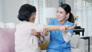 Young senior asia citizen female with scrubs nurse physiotherapy worker at home in rehabilitation therapy service for aging parents. Massage for older care, ache pain joints exercise in old people.