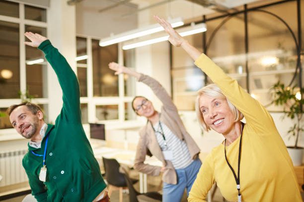 Cheerful active company employees in bright clothing exercising in office and making bending aside